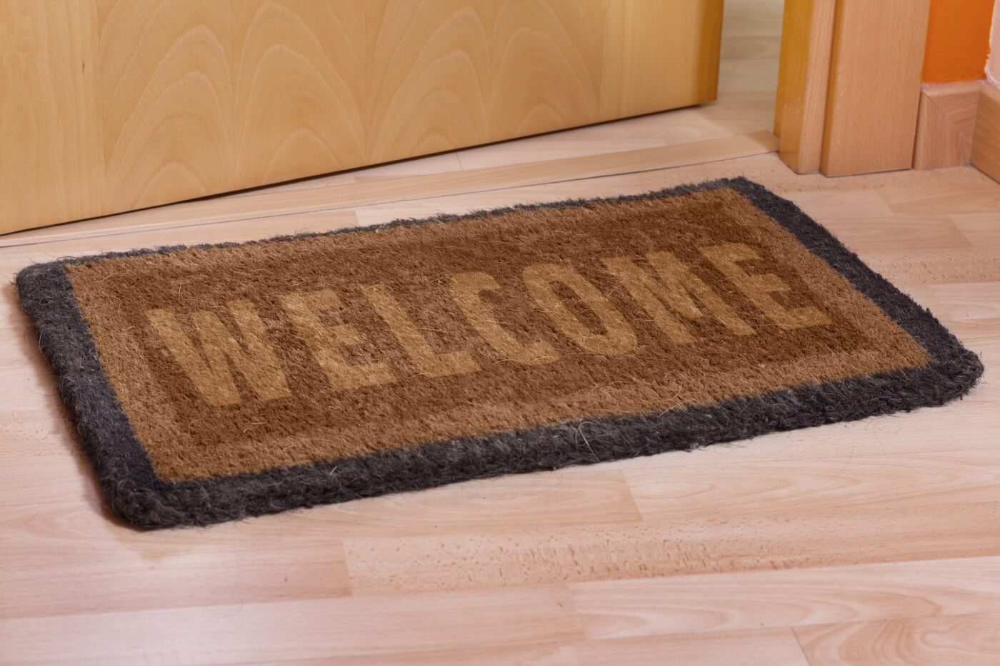 Hnedá rohožka pred dvere s nápisom Welcome. 