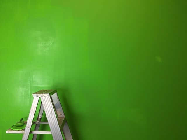 Rebrík na maľovanie pri zelenej stene. 