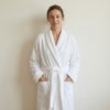standing woman wearing white frote terry bathrobe shawl style, wjth the background of creamy white wall @White terry bathrobe