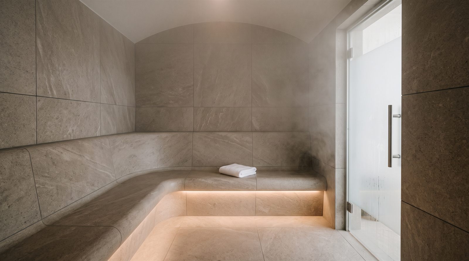 Moderná parná sauna v hotelovom wellness s lavicami z veľkoformátového kameňa, jemná para a zložený uterák