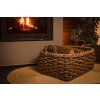 Vingo velký hnědý úložný ratanový koš s vyskládanými polínky stojící u zapáleného krbu ve večerní atmosféře.