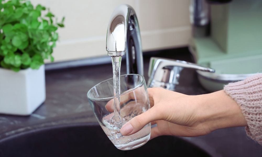 Nalievanie čistej vody z kuchynského kohútika do pohára – výsledok filtrácie reverznou osmózou