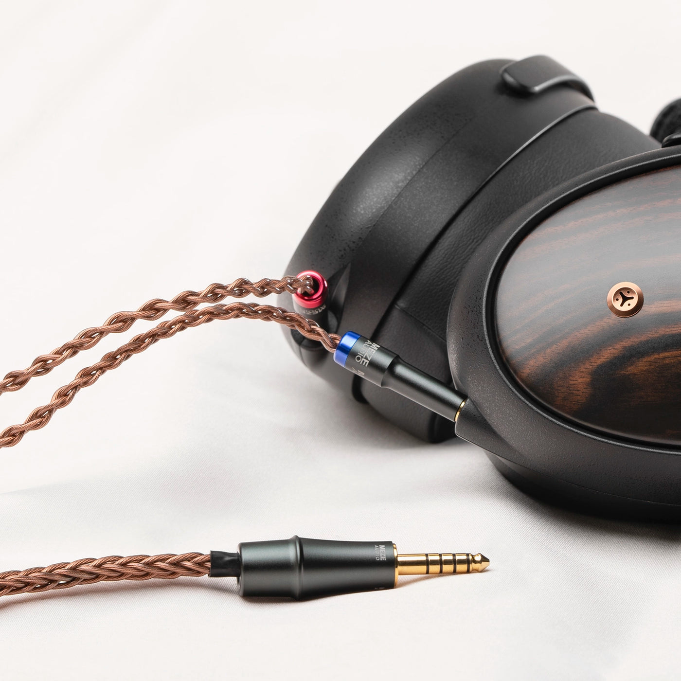 Měděný kabel Meze Audio Mono 3.5mm Copper PCUHD připojený k dřevěným sluchátkům Meze, v popředí pozlacené zakončení 4,4 mm