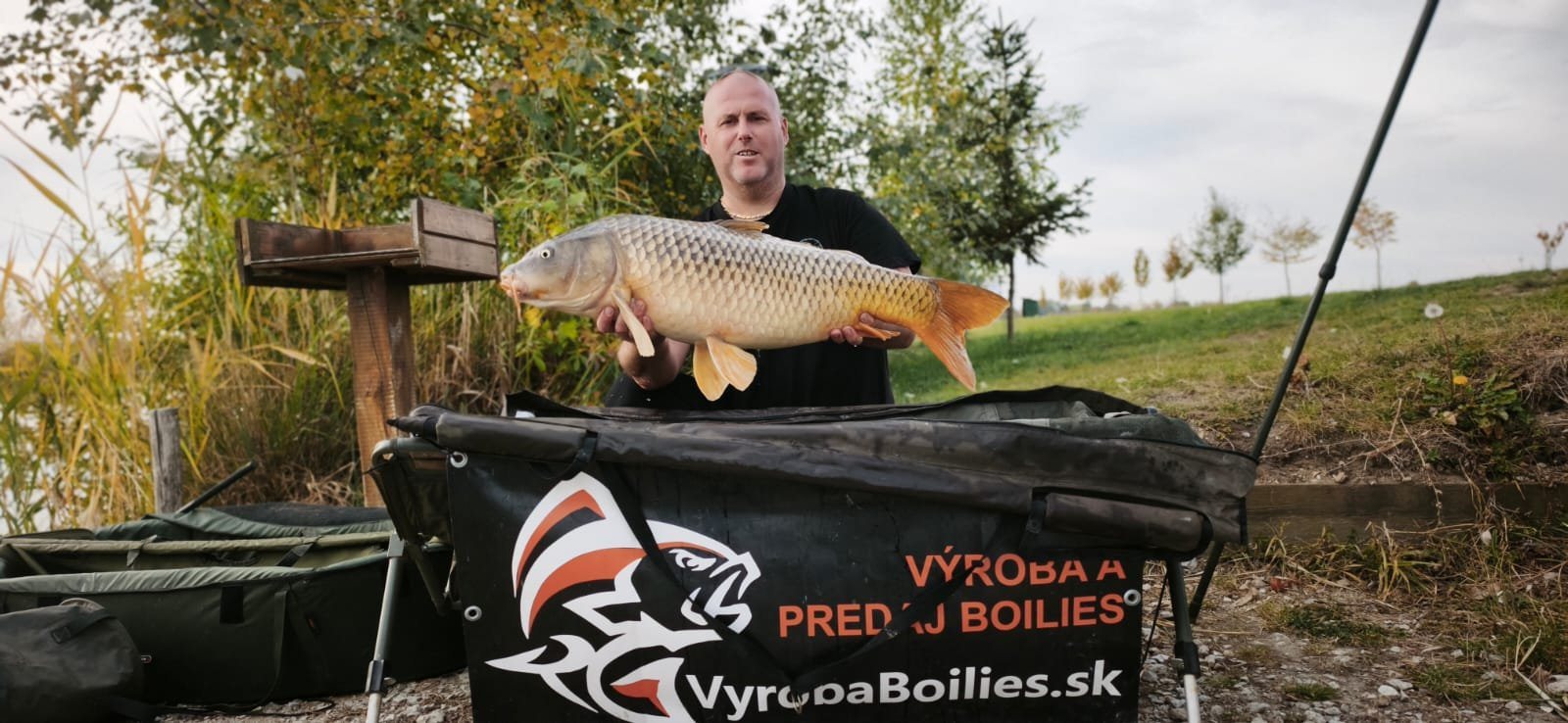 Rybár s kaprom pri banneri VyrobaBoilies.sk