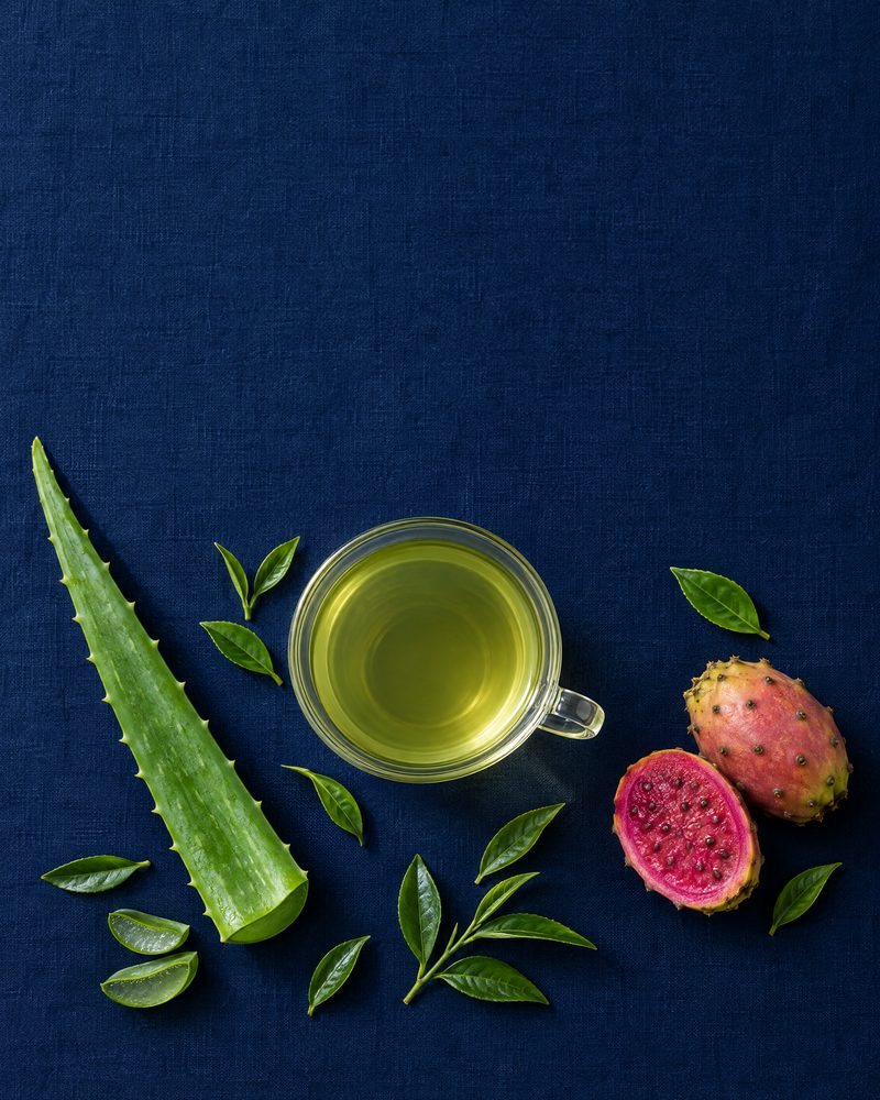 Šálek zeleného čaje s listem aloe vera a plody opuncie na tmavě modrém plátně