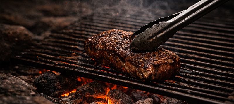 Hands cooking slowly over fire: stirring, basting, and turning food in warm light, focused and unhurried.