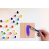 Bastelbrett wird mit violetter Farbe und Pinsel bemalt, Farbpalette im Hintergrund