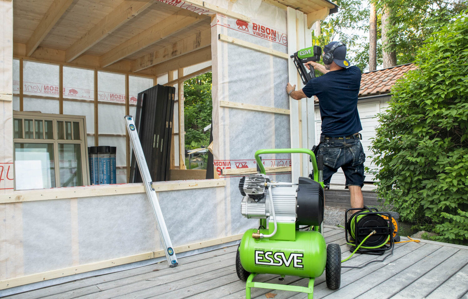 Muž pribíja zvislý fasádny obklad na rodinnom dome.