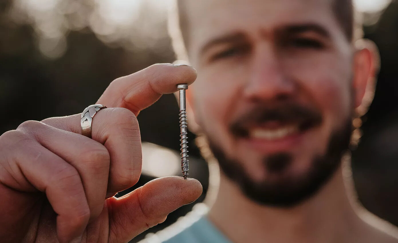 Stolár drží terasovú skrutku ESSDECK Max pred objektívom.